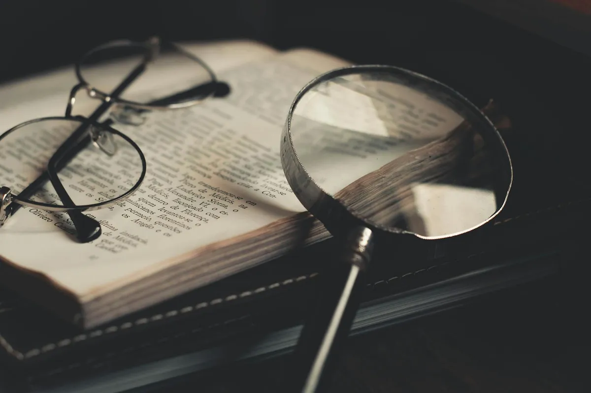 Close de livro aberto com lupa e óculos apoiados sobre as páginas