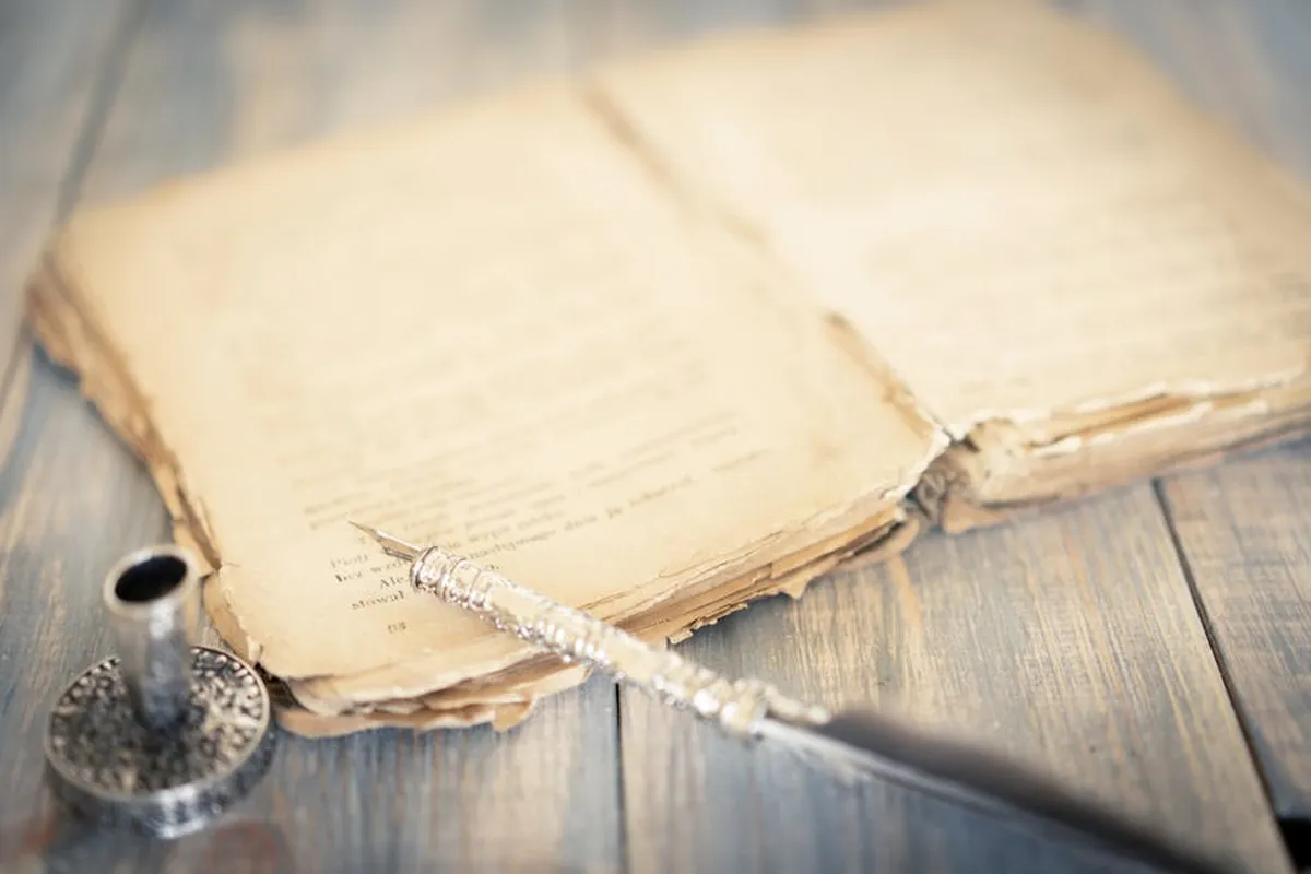 Livros antigos empilhados em mesa de trabalho com caneta sobre caderno