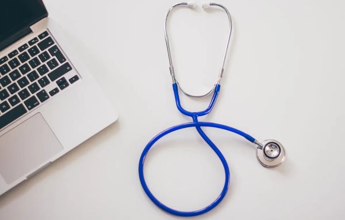 Estetoscópio médico e notebook sobre uma mesa branca, representando saúde digital
