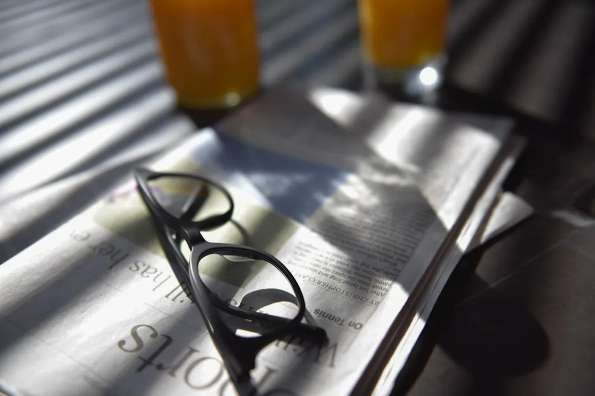 Óculos sobre um jornal aberto ao lado de copo de suco em luz natural