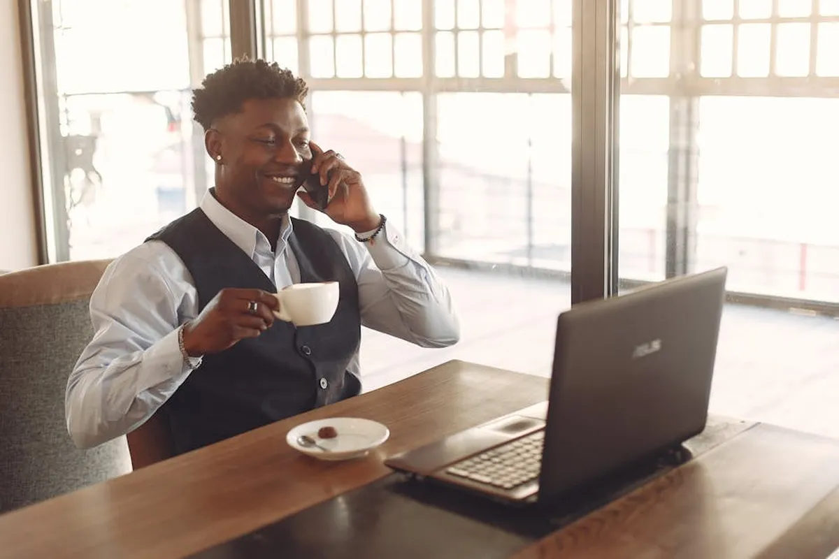 Profissional sorridente com café falando ao telefone num escritório moderno