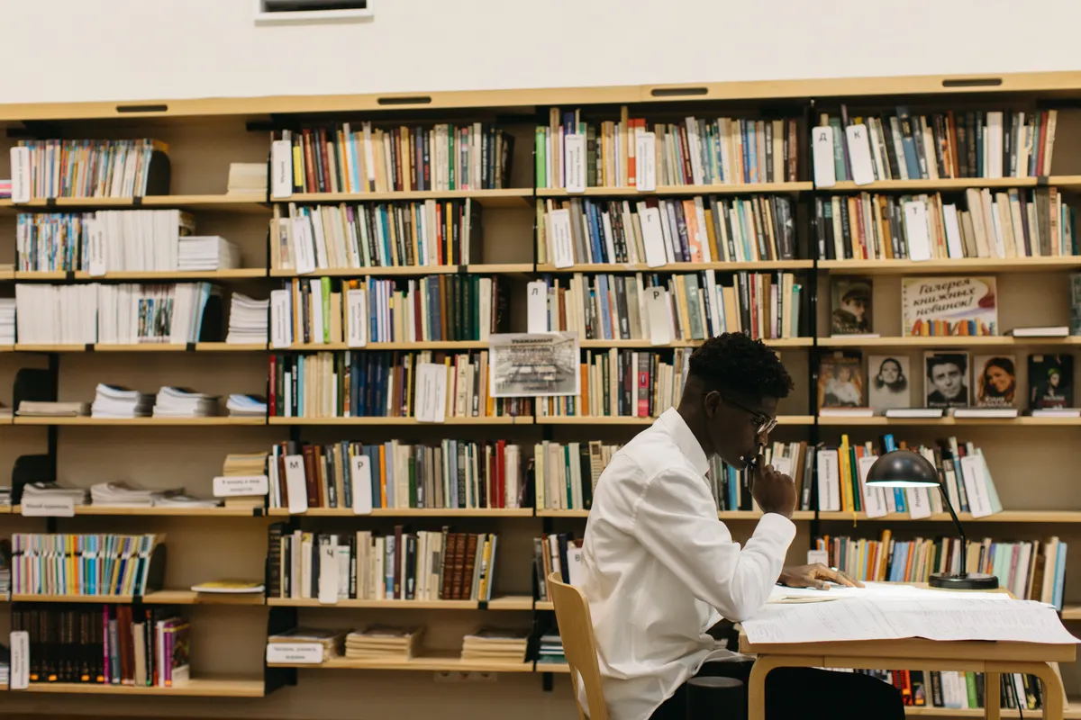 Estudante de pós-graduação sentada em uma mesa de estudos, olhando pensativa para o horizonte
