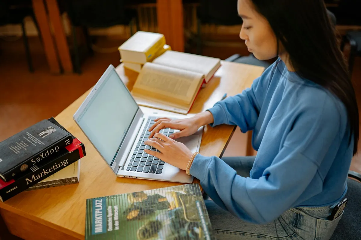 Estudante pesquisando programas de pós-graduação em laptop com caderno de anotações