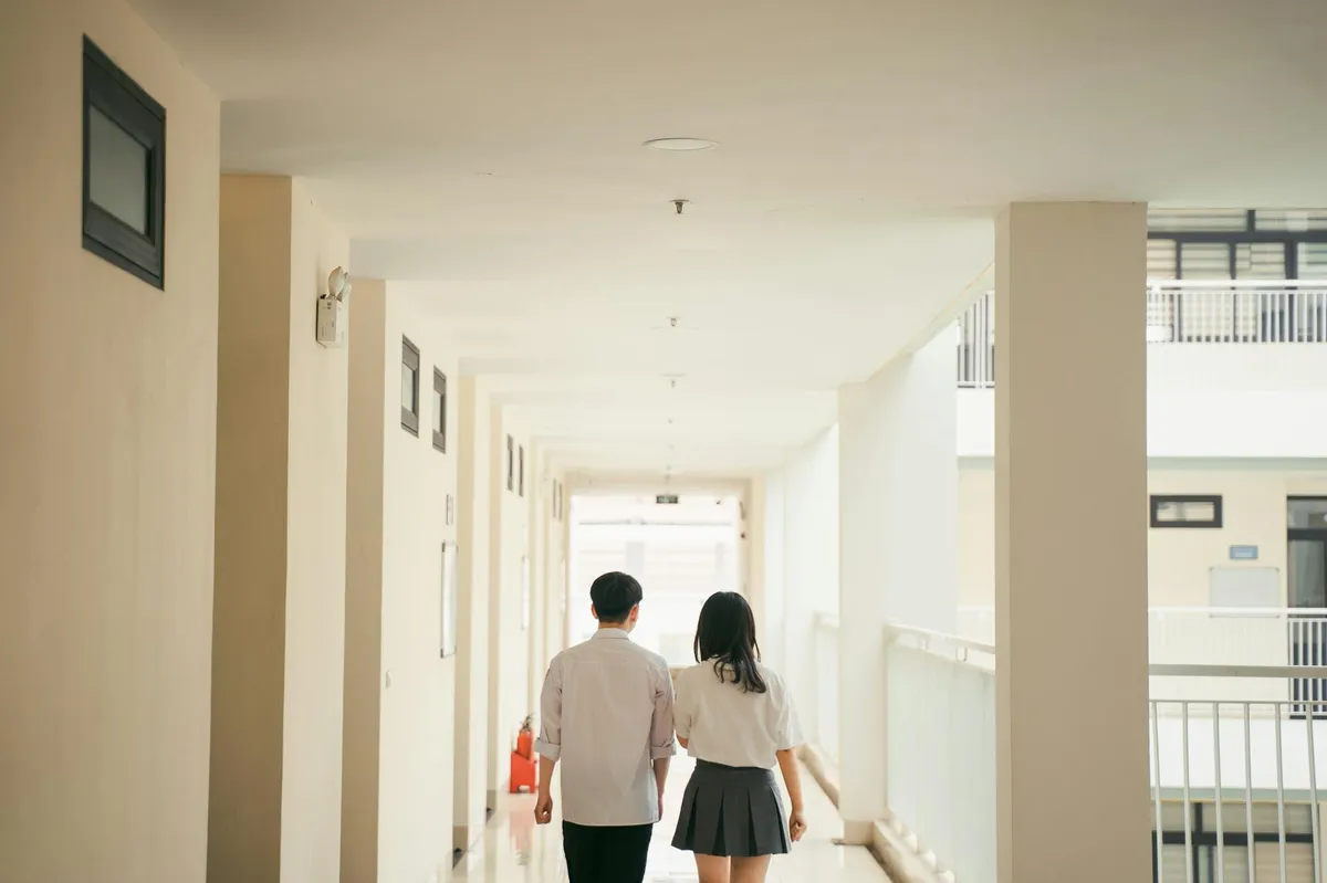 Corredor de universidade com pessoas caminhando, luz solar entrando pelas janelas