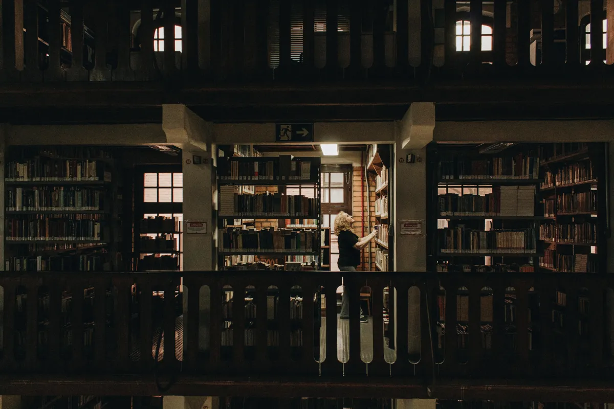 Pesquisadora lendo livros acadêmicos em biblioteca universitária