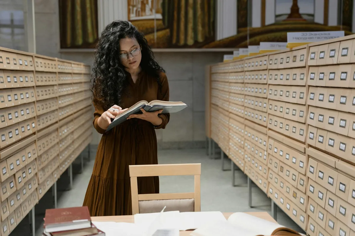 Pesquisador em biblioteca consultando livros e anotando em caderno para explorar tema