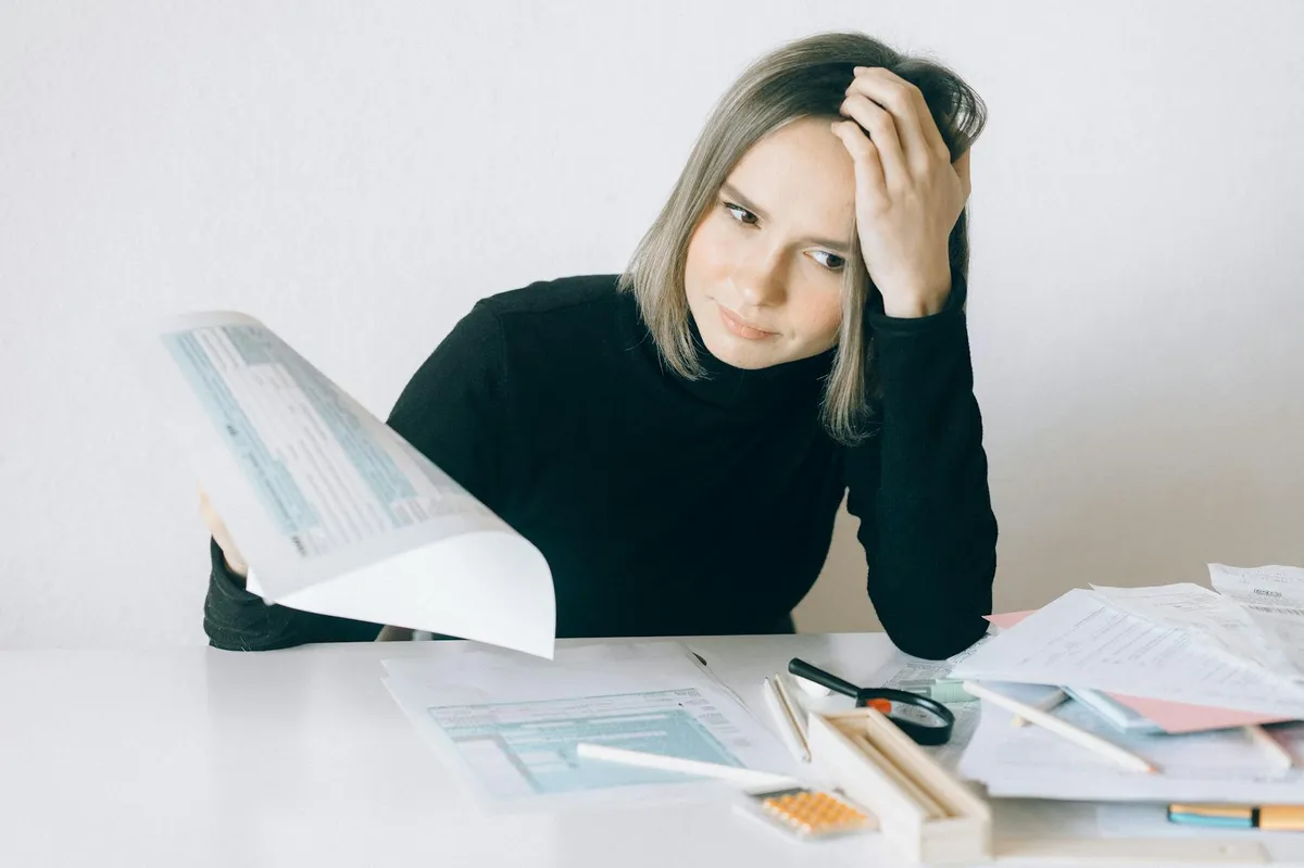 Pesquisadora estudando com expressão de cansaço e pilha de contas na mesa