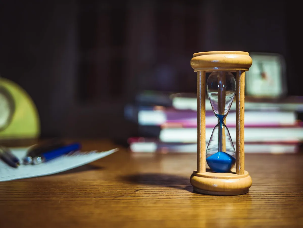 Pesquisadora usando timer na mesa de trabalho com livros e computador ao fundo