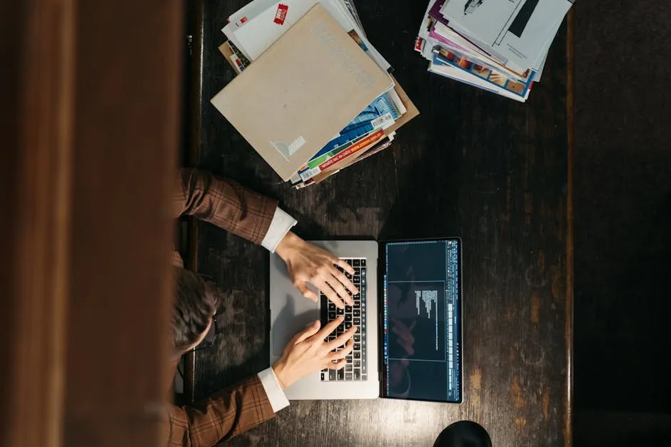 Mãos digitando em computador com documentos acadêmicos ao redor, representando escrita e ética acadêmica.
