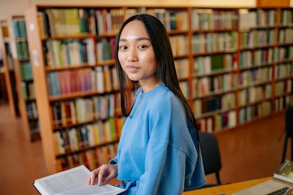 Jovem estudante em biblioteca olhando para livros com expressão determinada