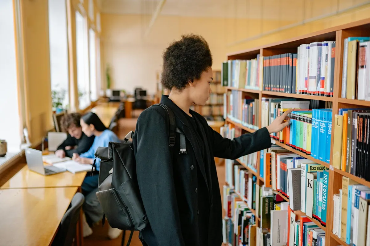 Estudante no início do mestrado com cadernos e livros em biblioteca universitária