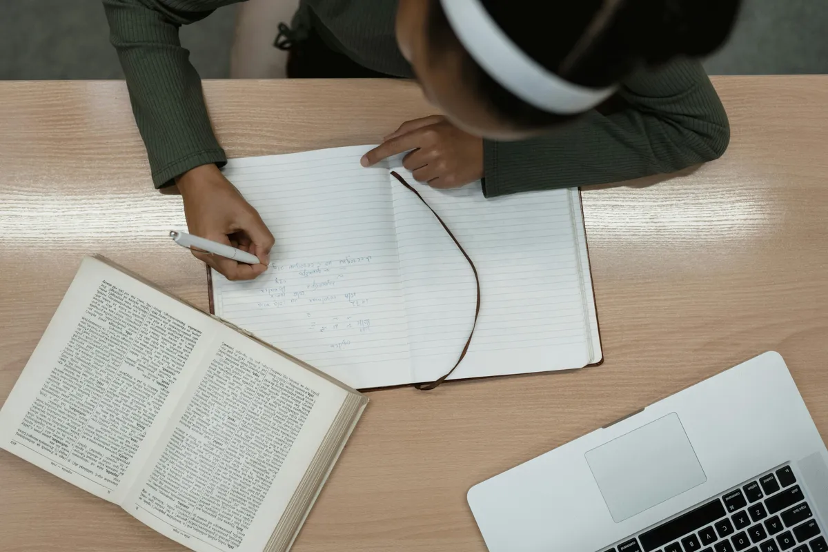 Estudante planejando projeto de pesquisa com caderno e computador em mesa