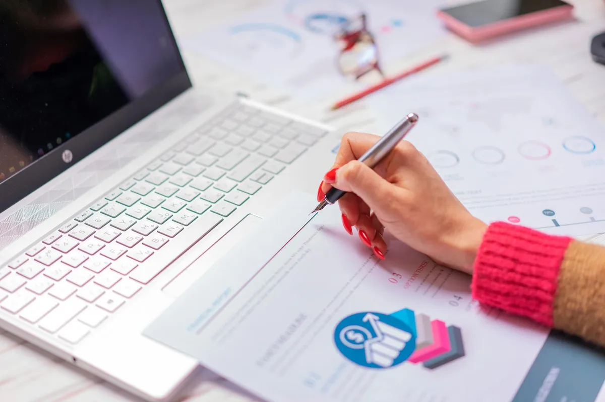 Estudante escrevendo relatório de estágio em caderno e laptop em mesa de escritório