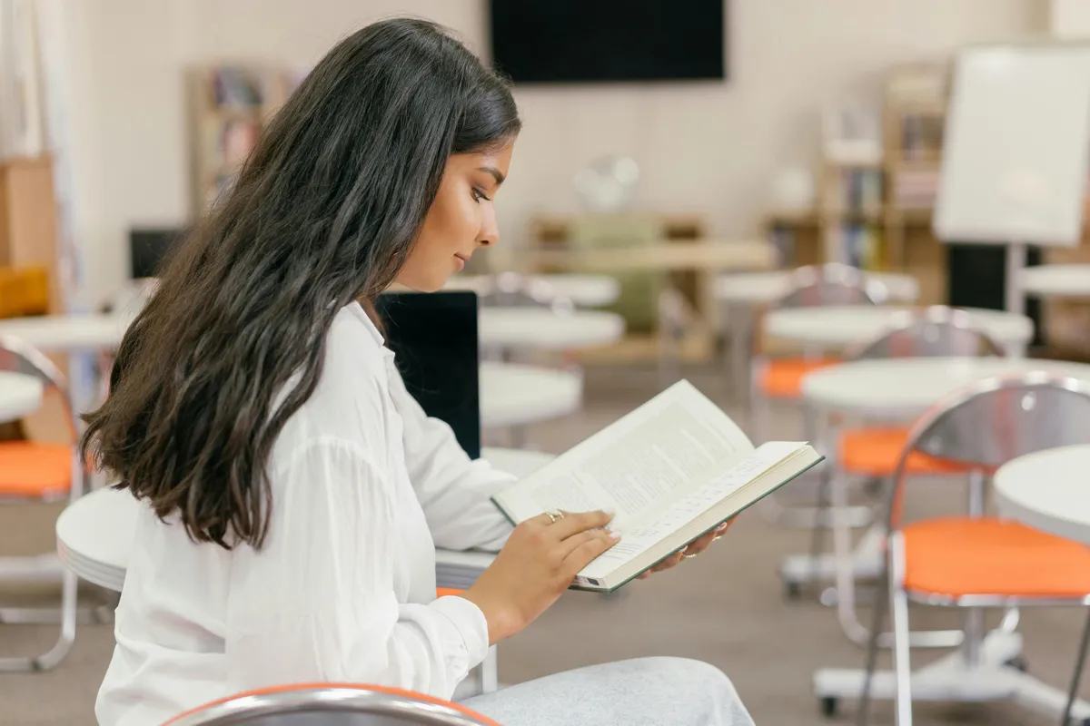 Estudante universitária fazendo anotações em livros acadêmicos para revisão bibliográfica