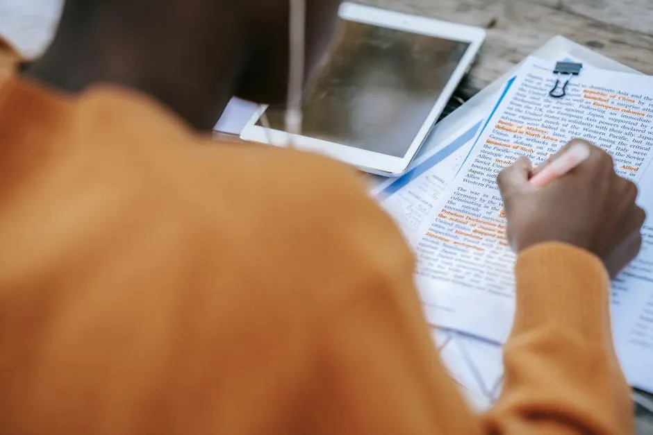 Pesquisadora consultando artigos científicos em tablet com caderno ao lado, representando busca em base de dados acadêmica.