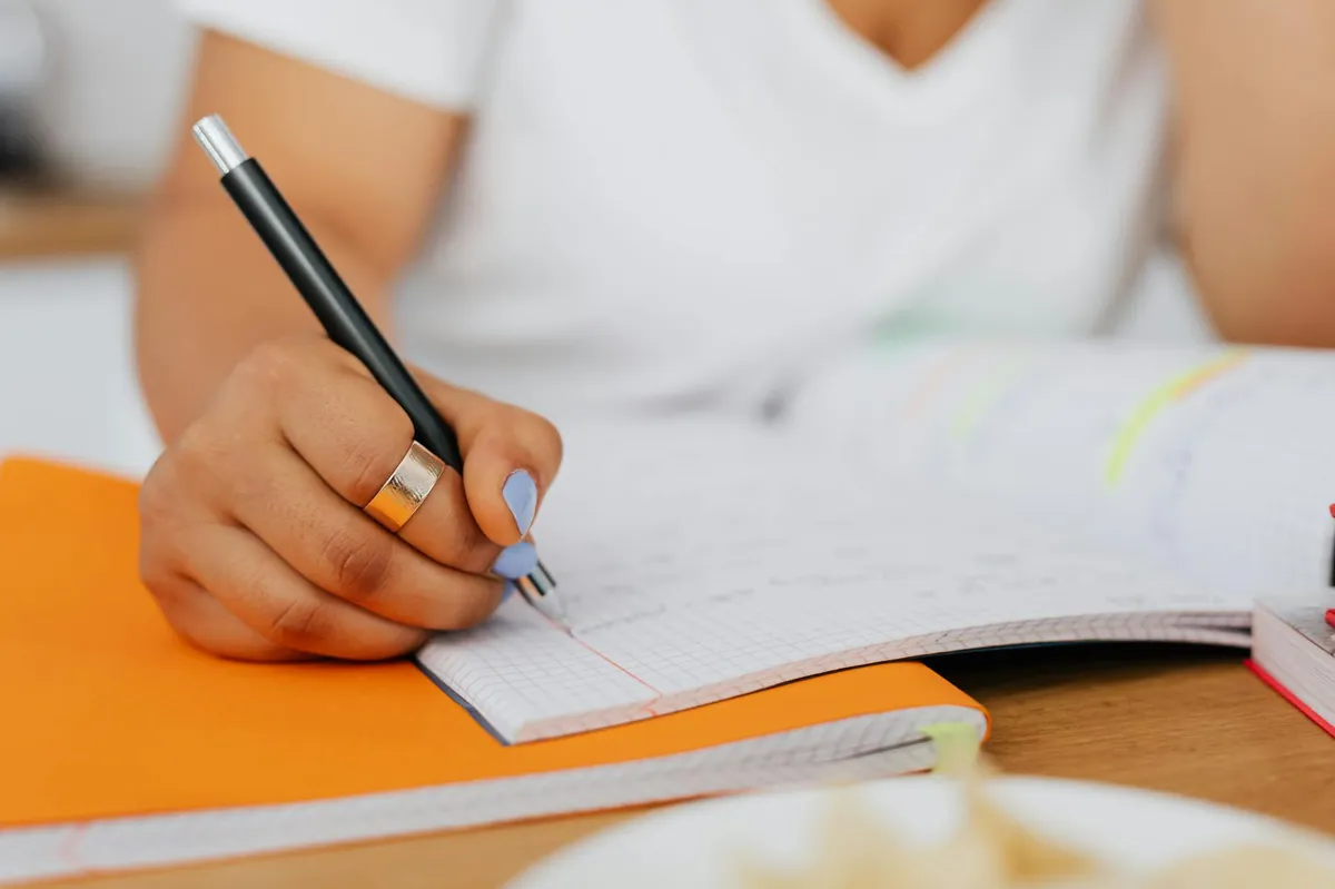 Profissional estudando e escrevendo seu TCC de especialização em uma mesa de trabalho
