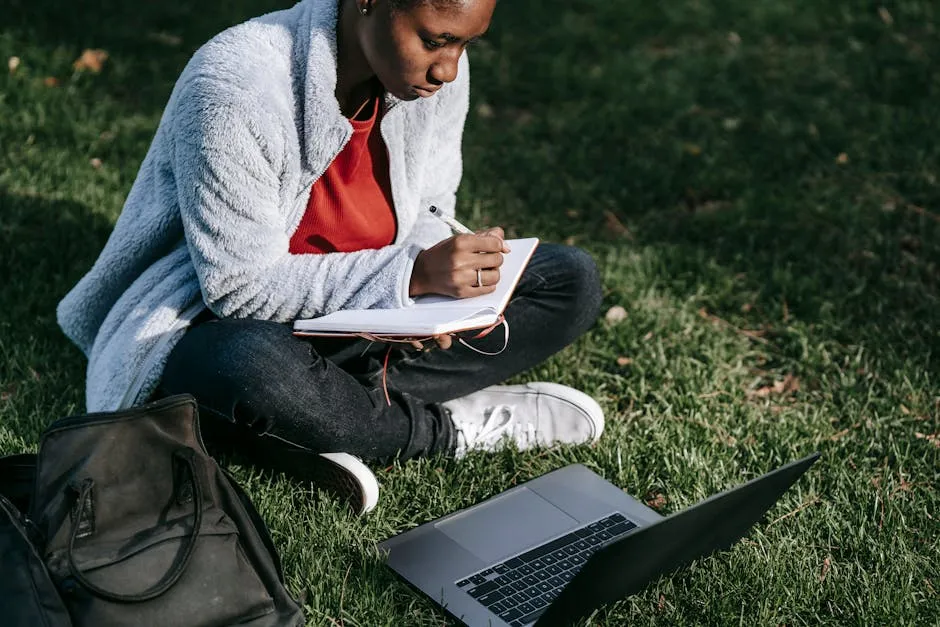 Estudante digitando TCC em notebook com cadernos e referências ao lado