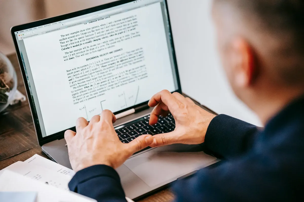 Pessoa lendo documento acadêmico em tela de computador com anotações ao redor