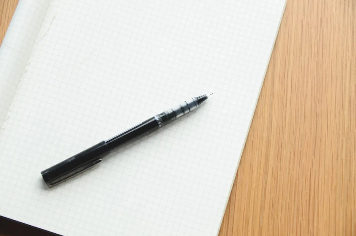 Caderno com texto acadêmico e caneta sobre mesa de madeira