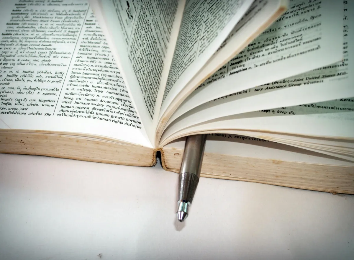 Pessoa estudando com dicionário e textos acadêmicos em diferentes idiomas sobre a mesa