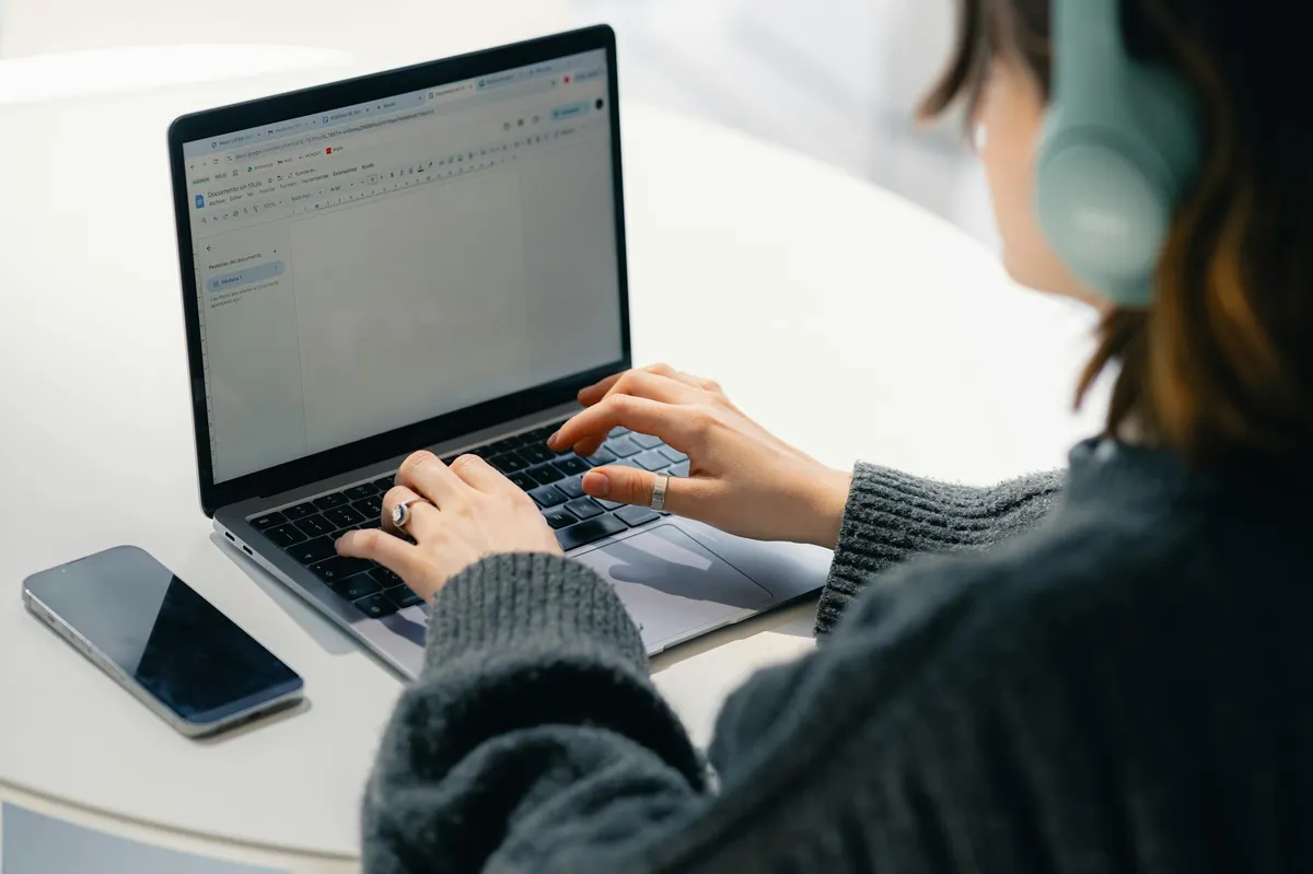 Pesquisadora com fones de ouvido digitando transcrição em computador portátil