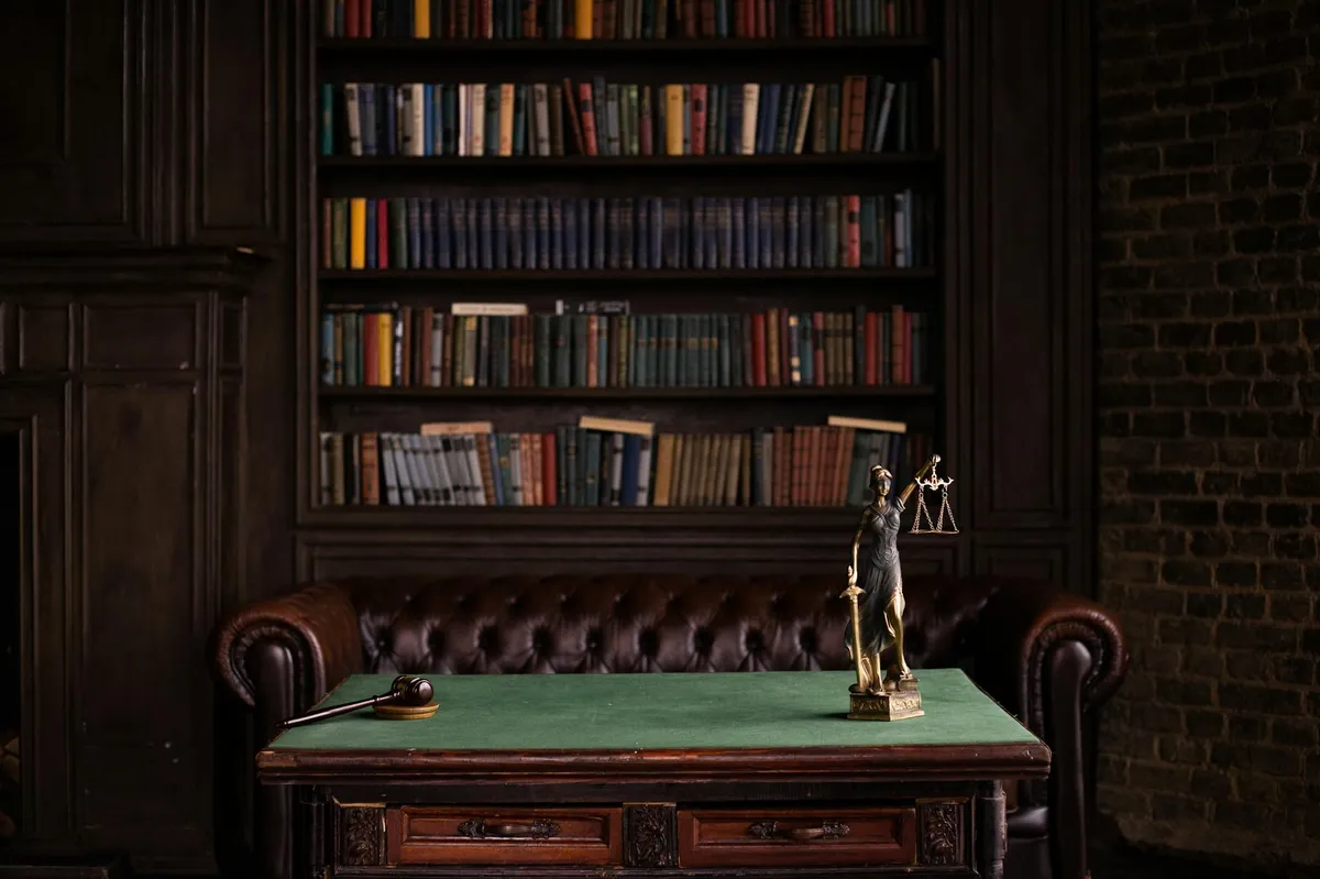 Sala de estudos com estantes de livros, martelo e estátua da Justiça sobre mesa verde