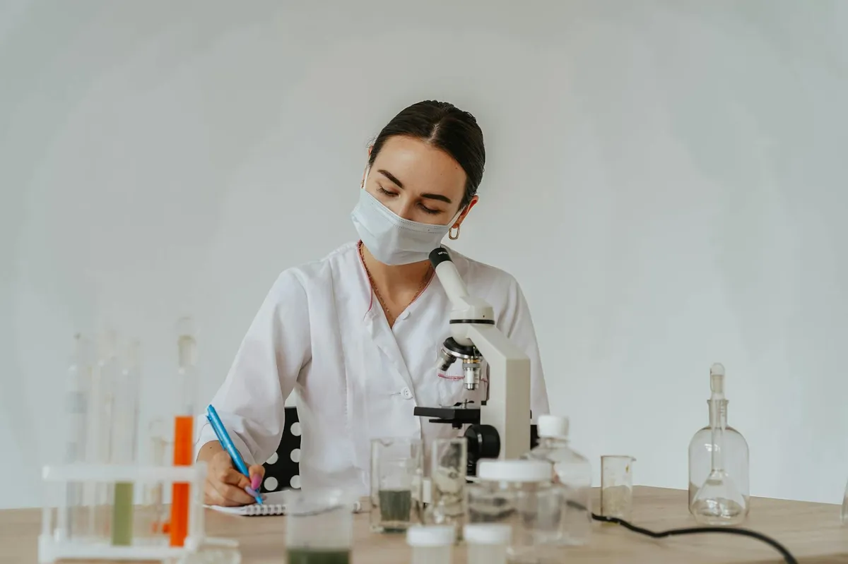 Pesquisador em laboratório analisando amostras ao microscópio e anotando resultados